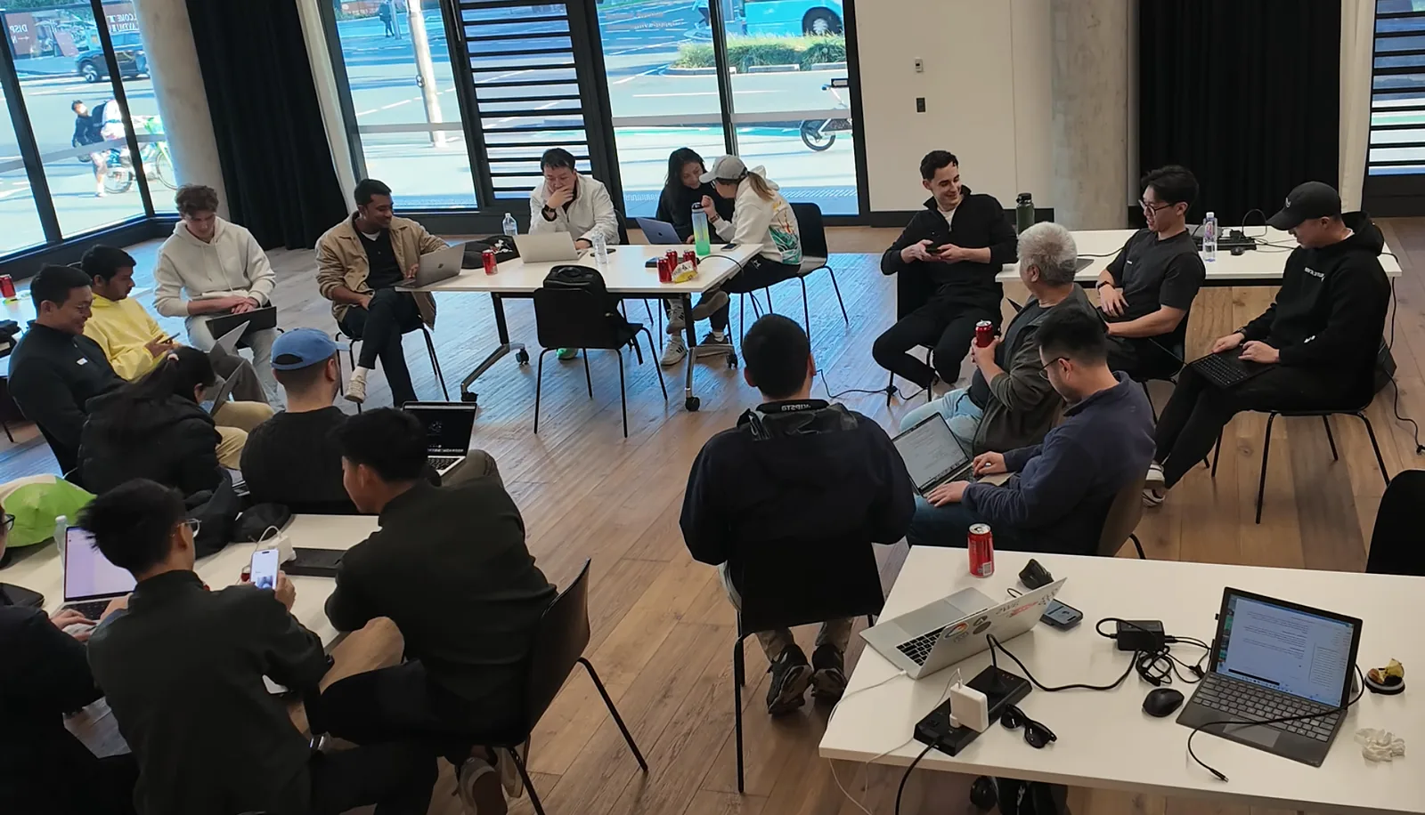 The room gathered in a wide circle of chairs and tables, laptops open, watching a demo.