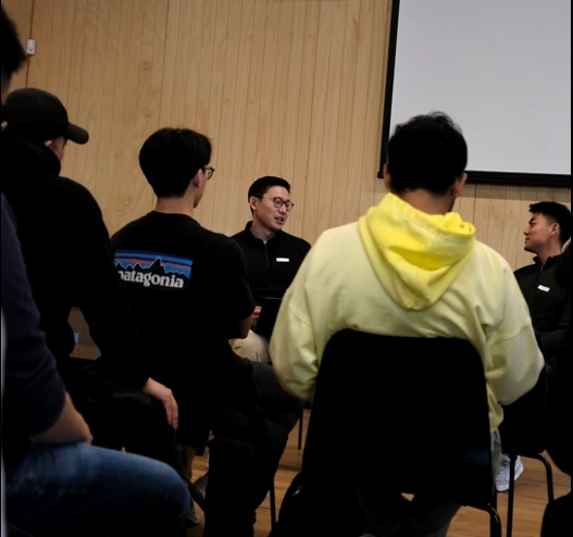 A seated room listens as one person speaks, viewed from among the audience.